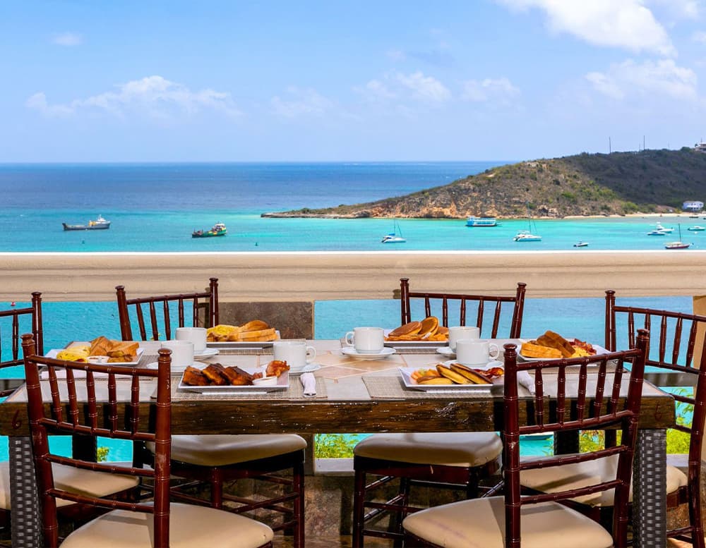 A beautifully set dining table overlooking a turquoise sea and a distant island.
